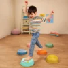 Chłopiec przeskakuje między kamieniami sensorycznymi Balance & Groove Set SOFT COLORS B. toys o nachylonych powierzchniach i różnych wypustkach